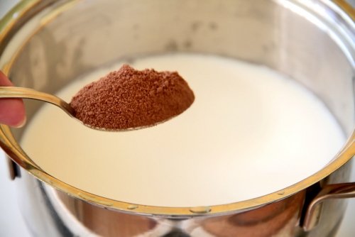 Молоко в кастрюльке, над ним ложка какао-порошка